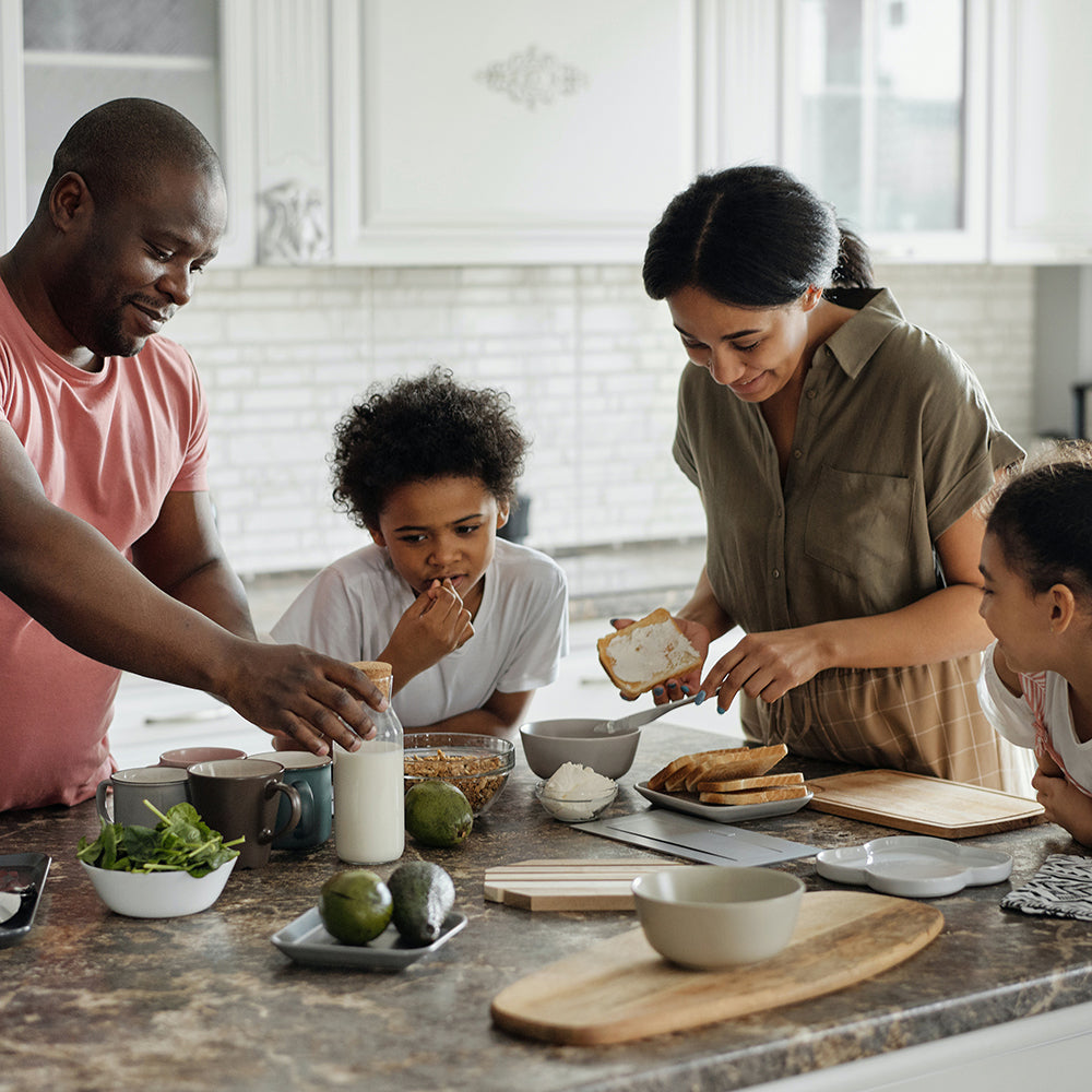 A family gathered around the kitchen island, cooking and enjoying bites of the food together.